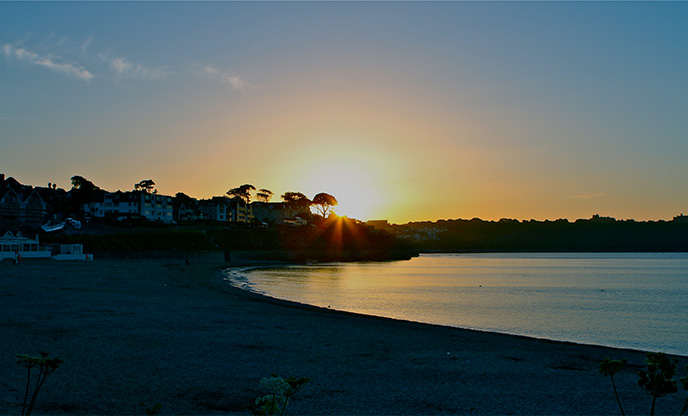 Sunrising over Gyllyngvase Beach in Falmouth with still waters and an azure sky