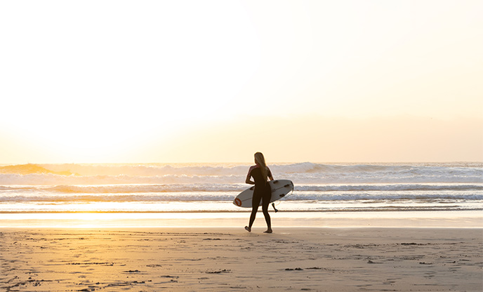 Woman walking into the sea with a surf board as the sunsets