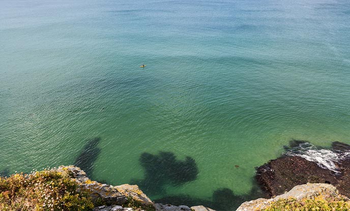 Looking down from the cliffs at Watergate Bay in Cornwall at a kayaker in the distance