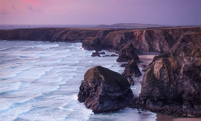 Pink hues fill the sky over impressive rock formations in the sea at Bedruthan Steps