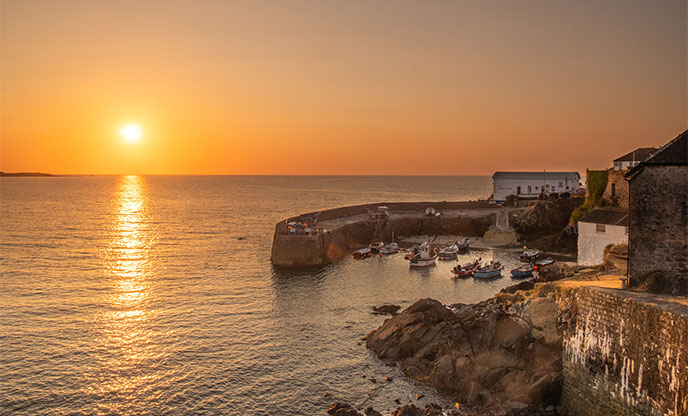 A golden sunrise over Coverack with fishing boats sat in the harbour 