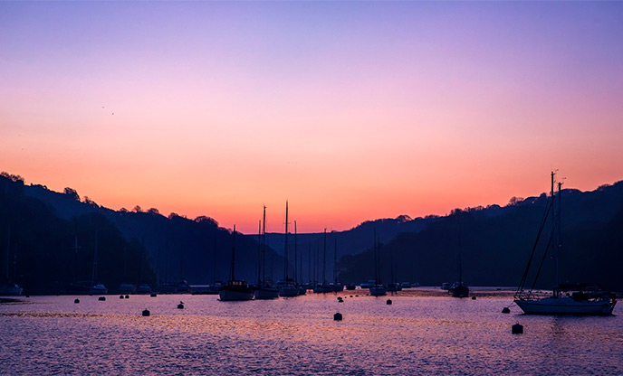 Purple and orange sunrise over Fowey Estuary with a silhouette of boats 