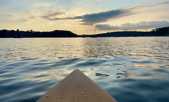 The tip of a wooden canoe as it sails up the Helford River in Cornwall at dusk