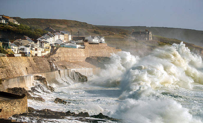 Massive waves crashing over the cliffs and houses at Porthleven, one of the best places to go storm watching in Cornwall
