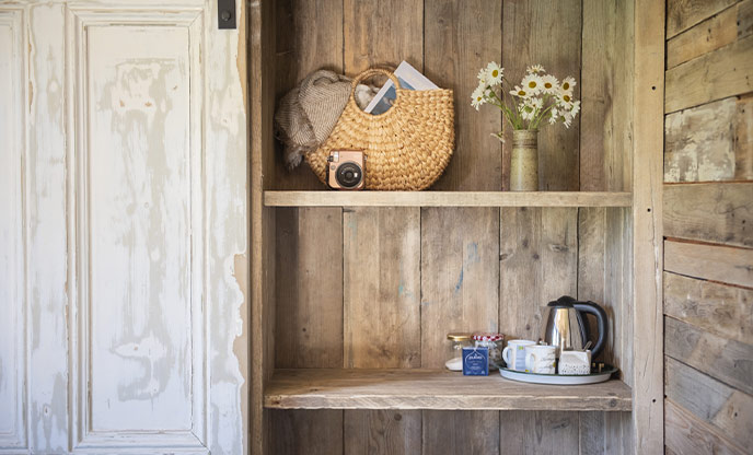 A wooden shelf at Clover Cabin in Cornwall with a polaroid camera and beach bag