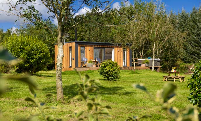 A small wooden cabin in a beautiful garden with trees in the background in Cornwall