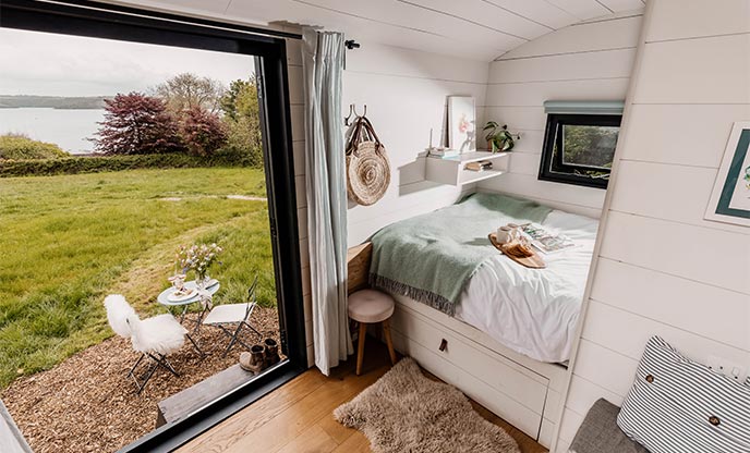 Inside of pretty shepherds hut looking out lush greenery and the glistening sea