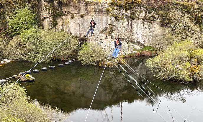 Two people going down a zip wire above the quarry at Via Ferrata in Cornwall