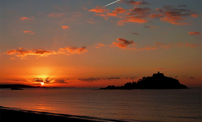 Crimson sunrise behind the silhouette of St Michaels Mount in Cornwall