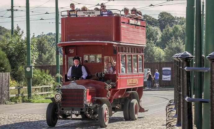An old-fashioned red bus with people on the top deck at Beamish Museum in County Durham