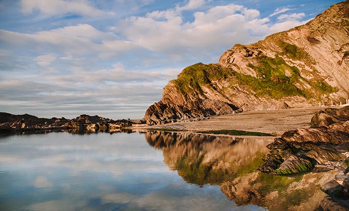 Rocks reflected in the glassy water of one of the pools at Tunnels Beach