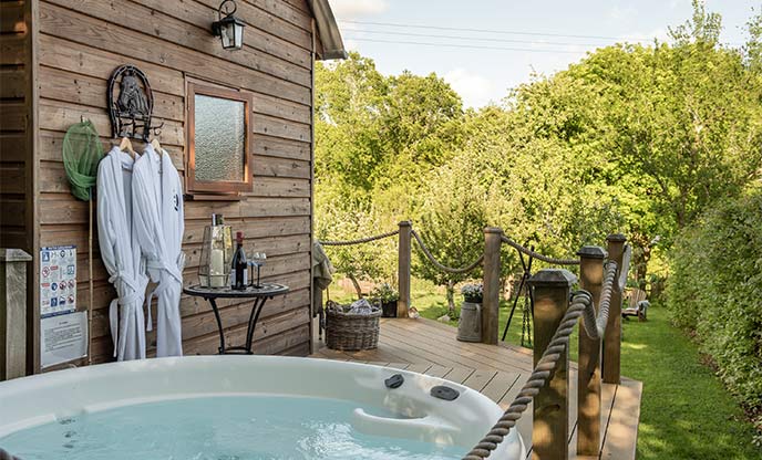 Secluded hot tub raised decking area surrounding shepherd's hut with lush green trees surrounding
