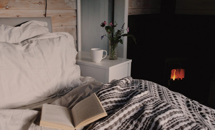 A bed next to a wood burner with an open book