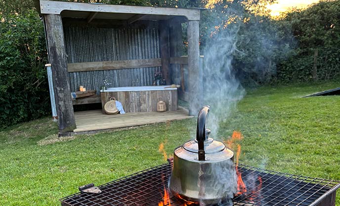 A silver kettle being heated over the flames of a fire pit.