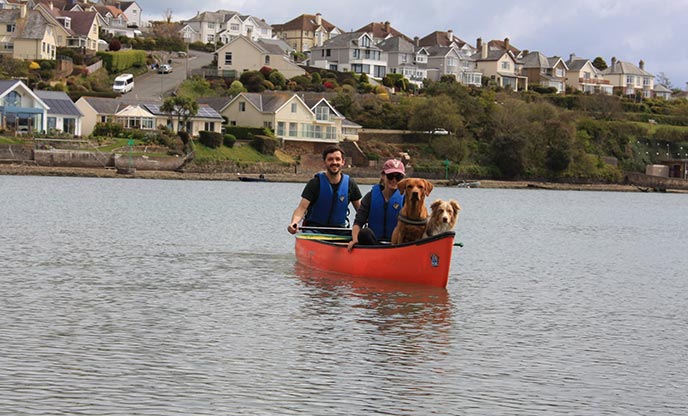 A couple and their dogs paddling away in a red canoe with Singing Paddles in Devon