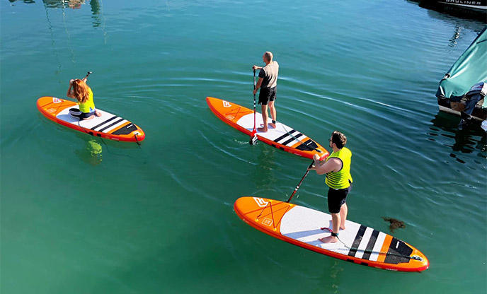 Three people stand-up paddleboarding at Torquay Harbour