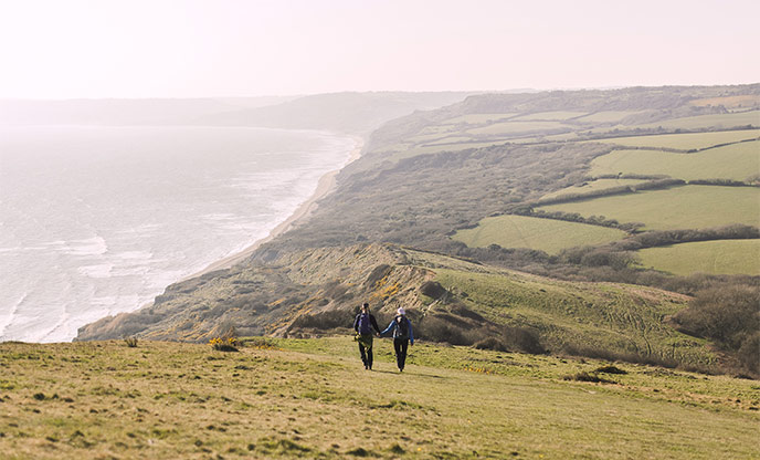 Couple walking hand in hand through fields along the Golden Cap coast path