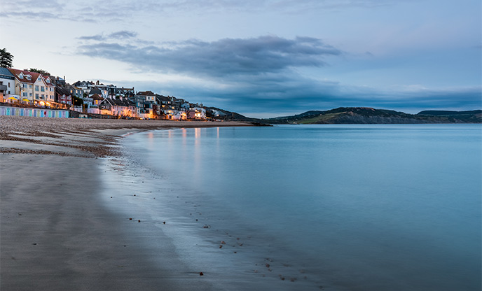 Evening at Lyme Regis beach, still water and vibrant buildings line the beach