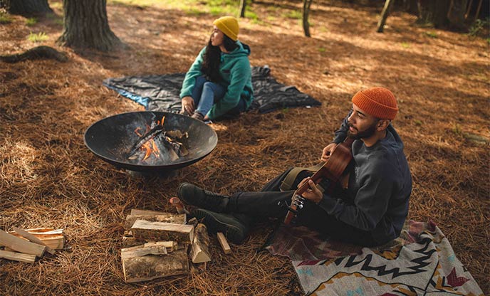 Couple gathered around a firepit in the forest playing the guitar