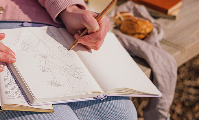 A person sketching flowers in a nature journal