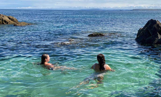 Two friends wild swimming in a crystal clear tidal pool in Cornwall