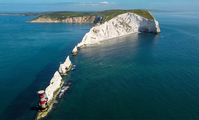 Ariel shot of The Needles on the Isle of Wight - towering white rock formations in the sea with a red lighthouse at the tip 