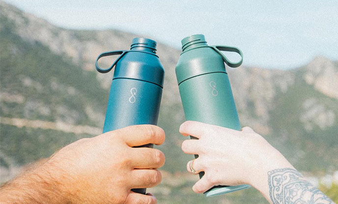 Two travel flasks with blue sky and mountain background 