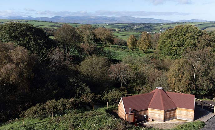 An aerial view of Cwt Mari, a cabin in Snowdonia (Eryri). The cabin is in the foreground with stunning mountains beyond it. 