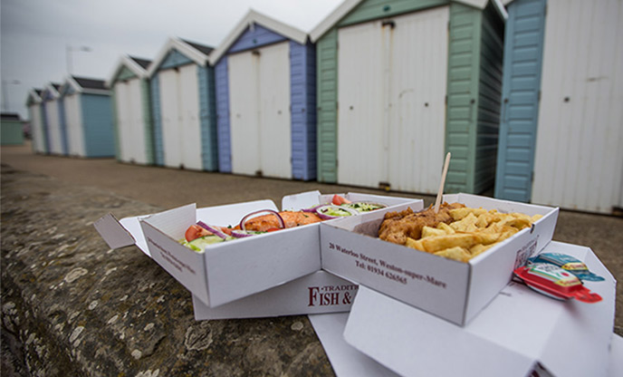 Takeaway fish and chips on the seafront with pastel coloured beach huts in the background