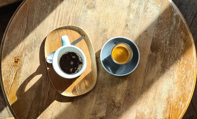 A black coffee and a latte shop from above on a wooden table