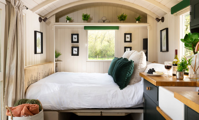 The bed at Douglas Fir shepherd's hut, it is covered in white linens with dark green accent pillows