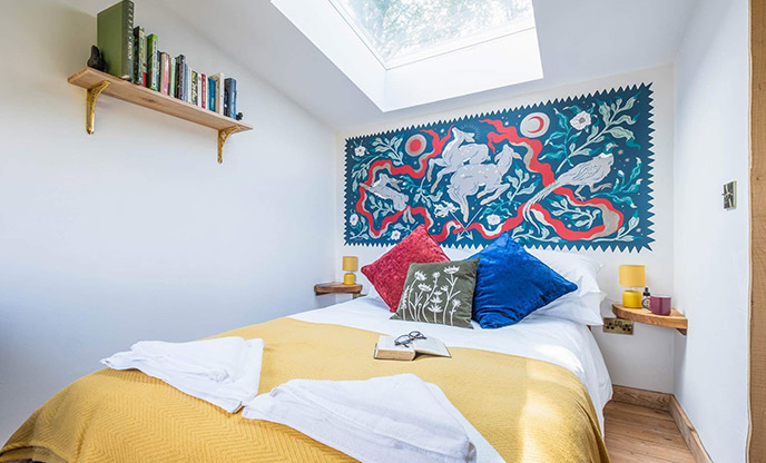 The bedroom at Matilda, a cabin in Sussex. The walls are painted white and there is a skylight in the ceiling above the bed.