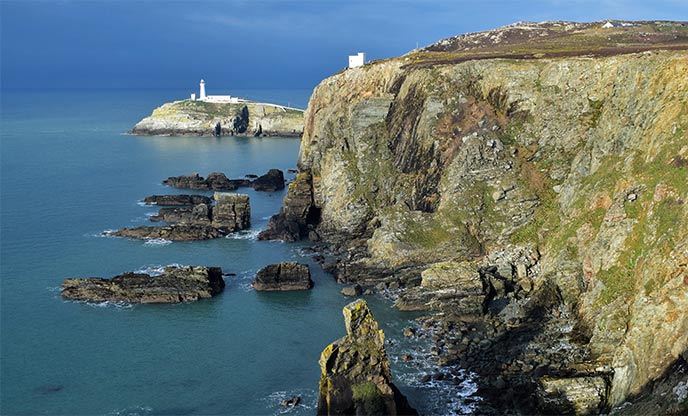 The rugged coastline in Anglesey looking out to the ocean and lighthouse