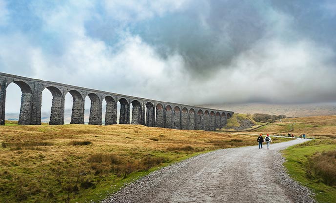 People walking along a footpath in the foreground of the Ribblehead Viaduct in Yorkshire